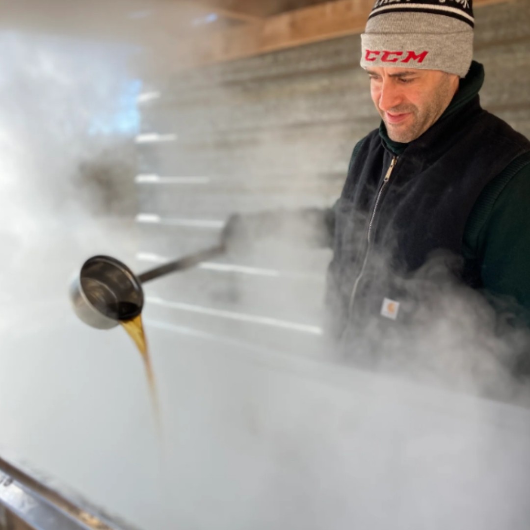 A man pouring maple syrup from a ladle is surrounded by steam at The Roost Farm's DIY Maple Syrup Experience.